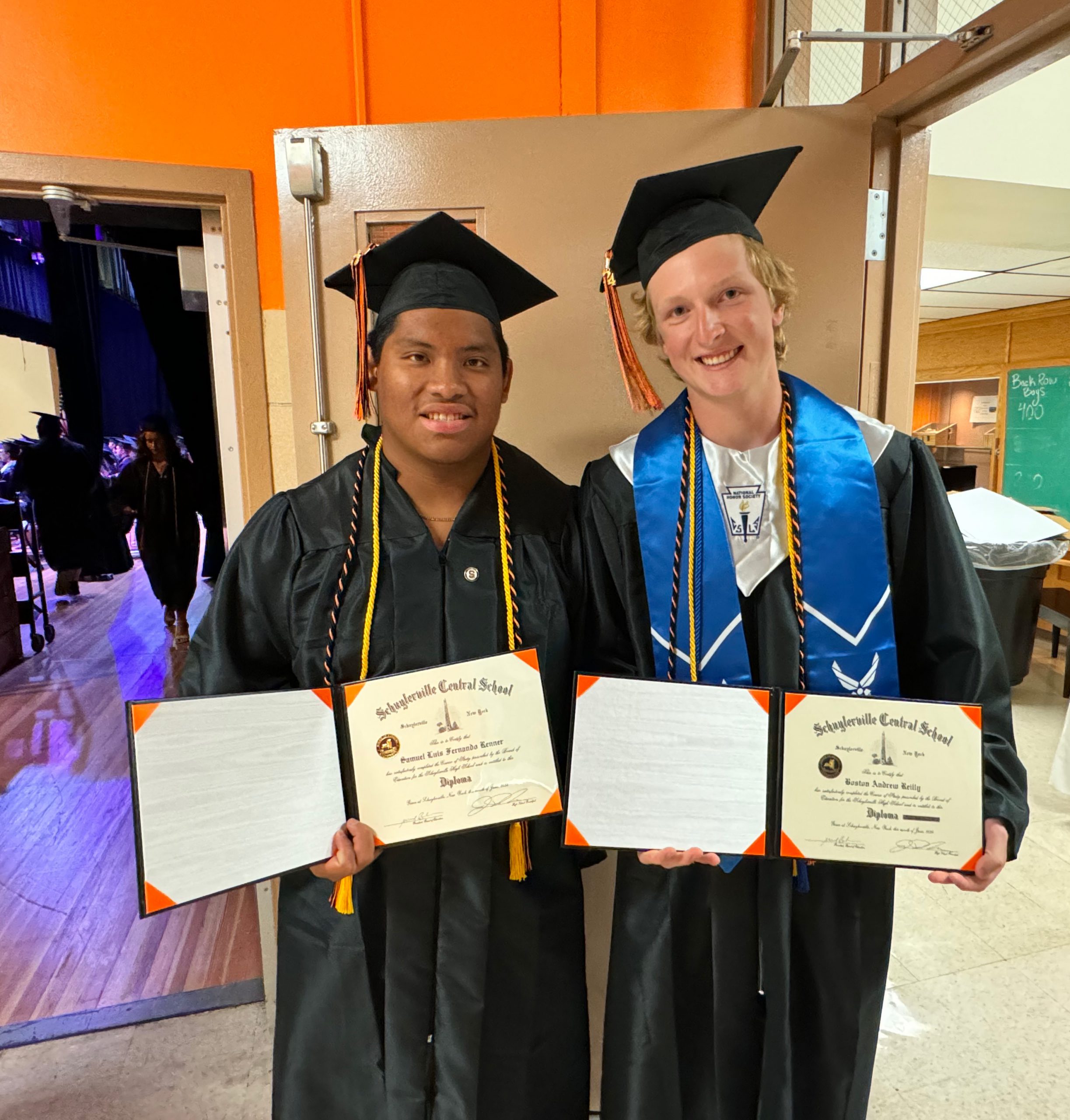 Two students proudly display their diplomas.